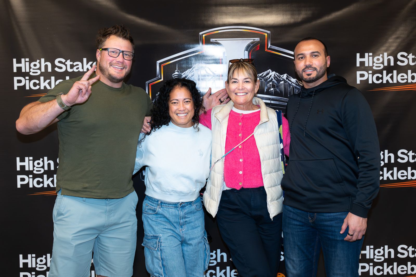 Four guests pose together in front of the High Stakes Pickleball backdrop, one making a peace sign.