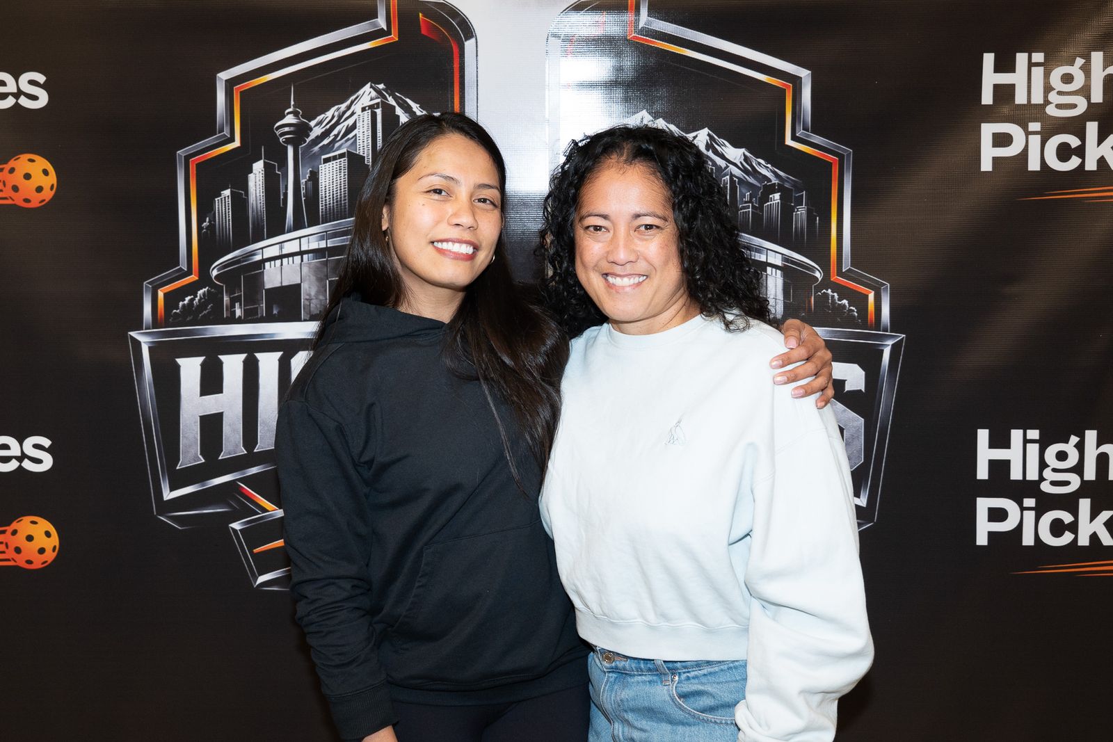 Two women pose with their arms around each other in front of the High Stakes Series logo on the backdrop.